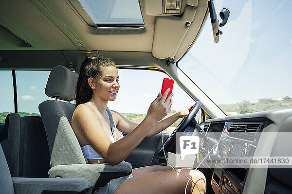 Lächelnde Frau checkt ihr Smartphone  während sie mit dem Wohnmobil fährt