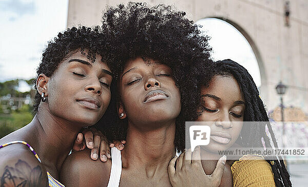 Young women with eyes closed leaning on shoulder's of female friend