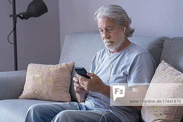 Senior man with in-ear headphones using mobile phone at home