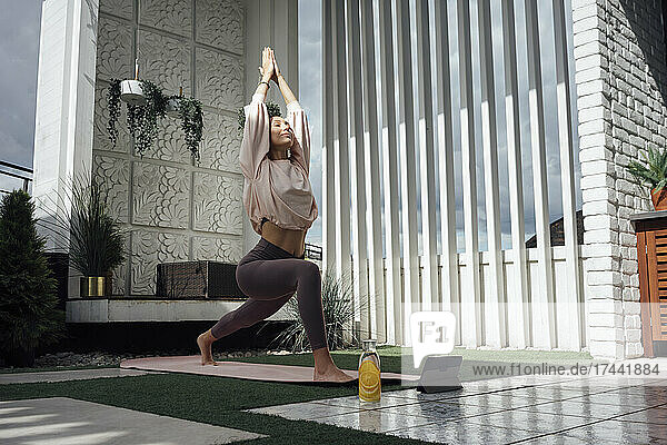 Mid adult woman with hands clasped stretching legs while practicing yoga on terrace