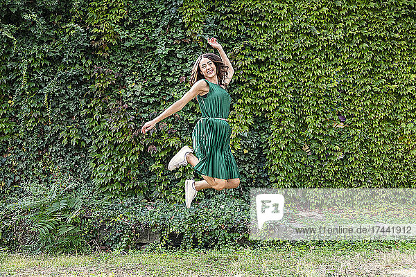 Unbeschwerte Frau springt vor grünen Efeupflanzen