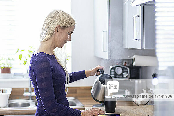 Frau gießt heißes Wasser in eine Tasse  während sie zu Hause in der Küche Kaffee zubereitet