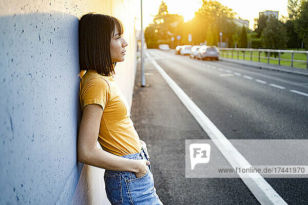 Thoughtful woman with hand in pocket leaning on wall