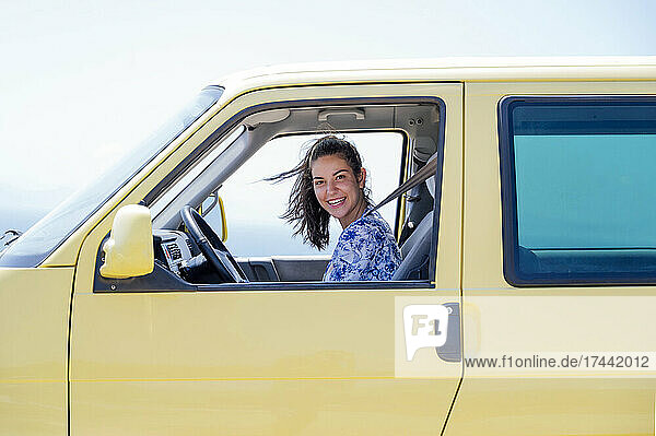 Happy mid adult woman sitting in yellow camper van during sunny day