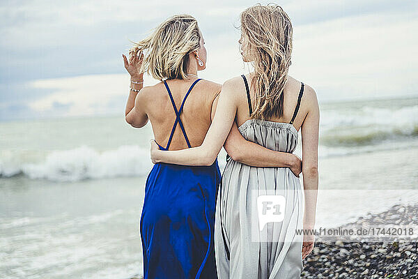 Mother and daughter in cocktail dress with arms around walking on beach
