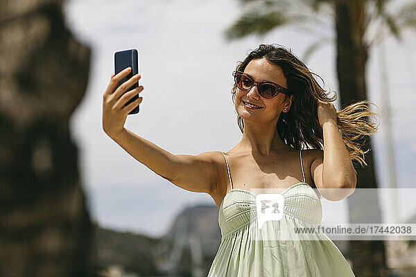 Mid adult woman with hand in hair taking selfie through smart phone