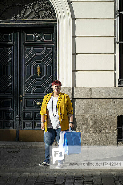 Lächelnde Frau mit Einkaufstasche steht auf Fußweg