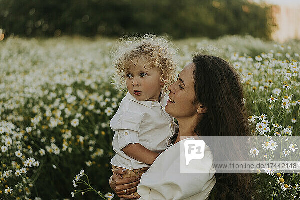 Smiling woman carrying blond baby boy at field