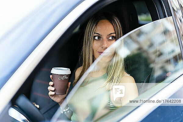 Blonde Frau mit Kaffeetasse schaut durch das Autofenster