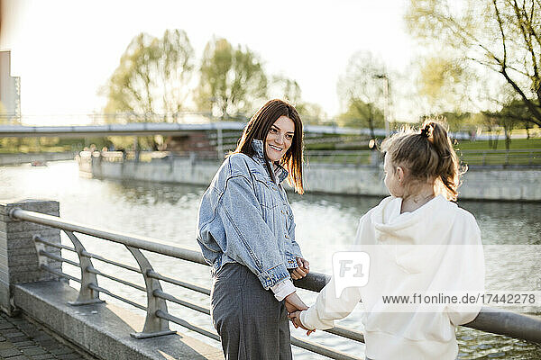 Smiling mother holding daughter's hand at embankment