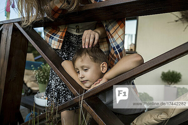 Mother stroking son leaning on wooden railing