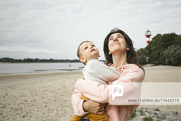 Mother with son looking up while standing at beach
