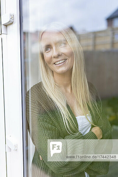 Woman with arms crossed looking through glass in house