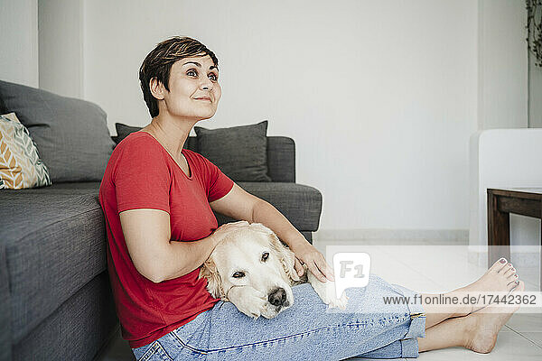Thoughtful mid adult woman sitting with Golden retriever at home