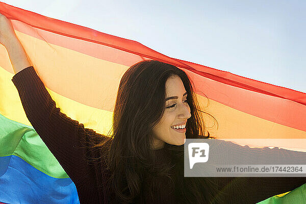 Young woman looking away while holding rainbow flag