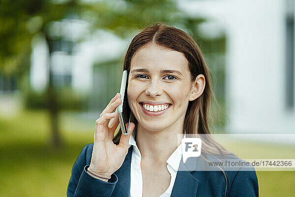 Happy young businesswoman with brown hair talking on mobile phone