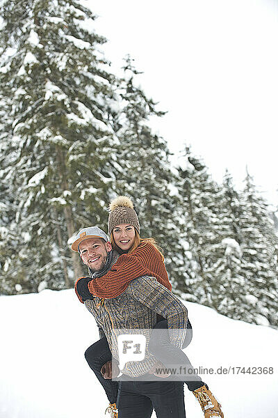 Smiling mid adult man giving piggyback ride to woman during winter