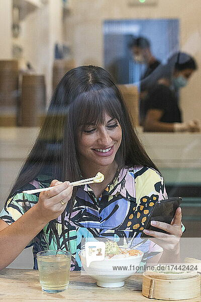 Woman using mobile phone while having food at restaurant