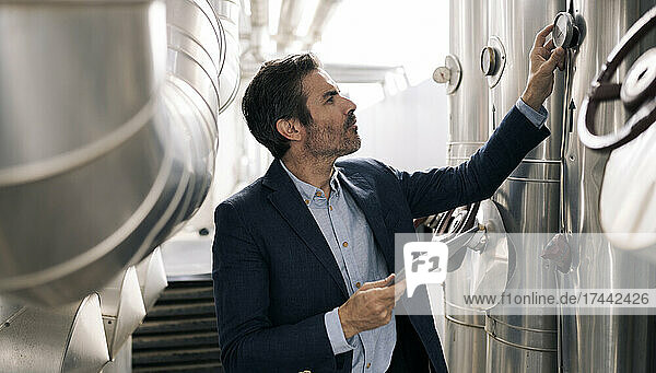Businessman holding digital tablet while examining machinery at industry