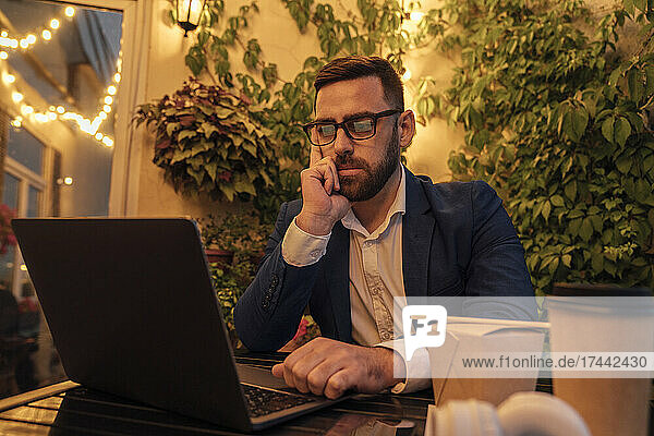 Thoughtful businessman looking at laptop in office balcony
