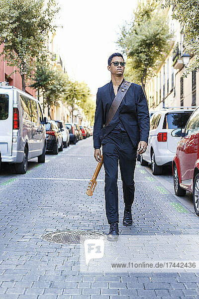 Young male musician with guitar walking on street