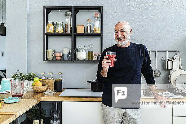 Happy man holding smoothie glass in kitchen