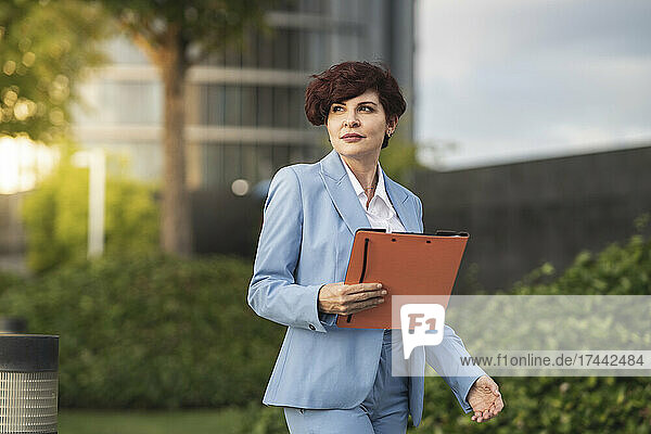 Beautiful businesswoman with file walking at office park