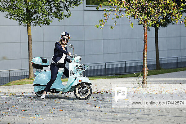 Smiling businesswoman riding motor scooter