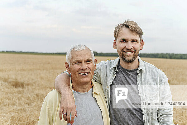 Lächelnder Sohn mit dem Arm um den älteren Vater auf dem Feld