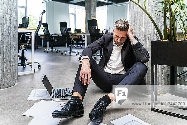 Businessman with head in hand sitting on floor in office