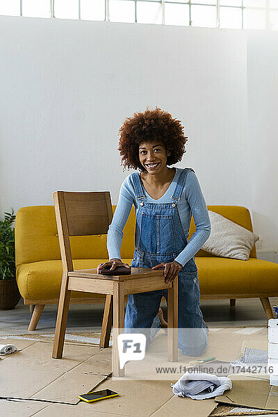 Smiling Afro woman polishing wooden chair in living room