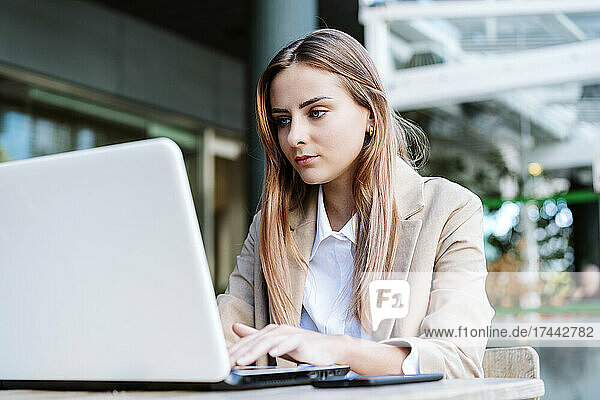 Female business professional using laptop at cafe terrace