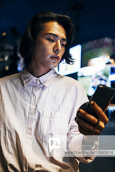 Young man with smart phone in city at night