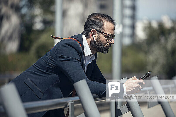 Männlicher Geschäftsprofi benutzt Mobiltelefon  während er sich an das Geländer lehnt