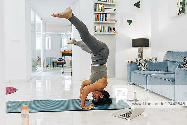 Female vlogger doing headstand while filming home workout tutorial in living room