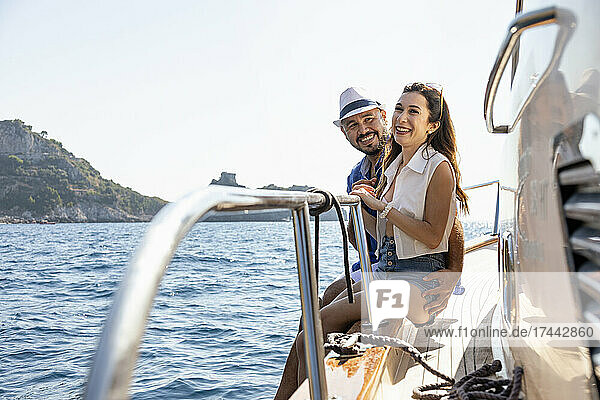 Smiling couple sitting at motorboat edge during sunny day