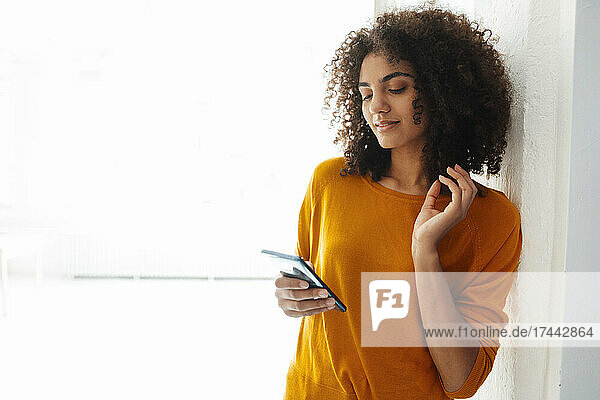 Afro young woman text messaging through smart phone at home
