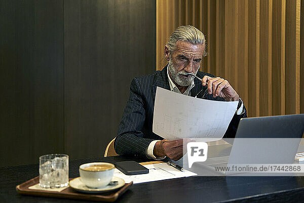 Reifer Geschäftsmann liest Dokument  während er am Schreibtisch sitzt