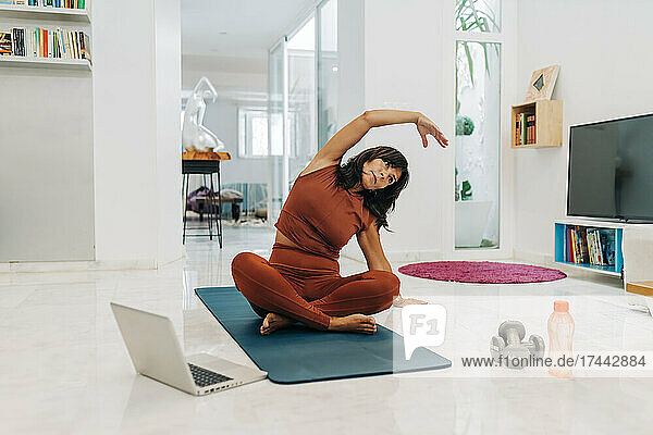 Aktive Frau praktiziert Yoga beim E-Learning per Laptop zu Hause