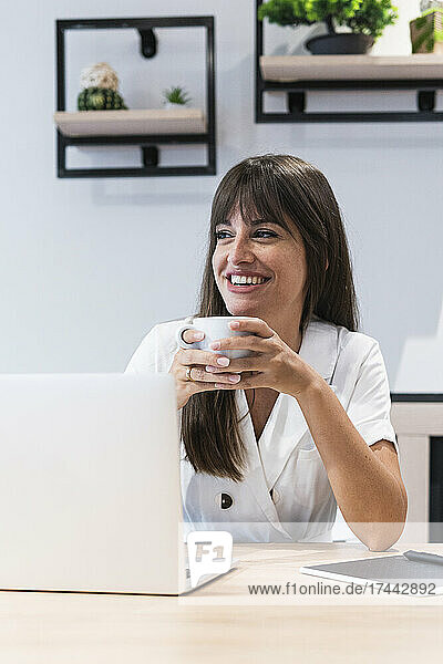 Happy businesswoman with laptop having coffee at restaurant
