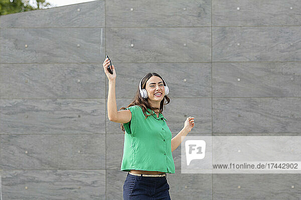 Happy woman dancing in front of gray wall