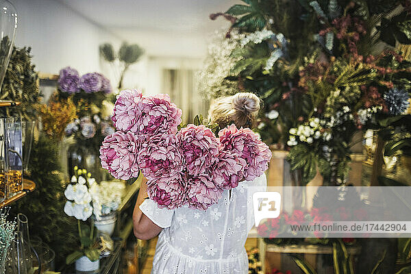 Floristin trägt rosa Blumenstrauß  während sie im Geschäft arbeitet