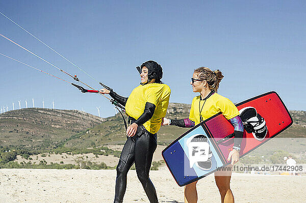 Smiling female instructor holding kiteboard while instructing to woman during sunny day