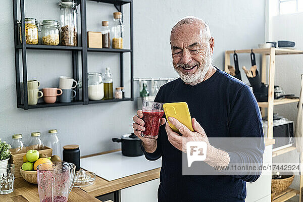 Man with smoothie glass using mobile phone at home