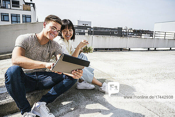 Smiling male and female friends using digital tablet on sunny day