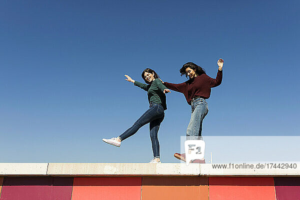 Female friends dancing on retaining wall
