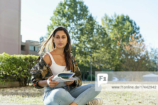 Female teenager holding book while sitting cross-legged in park