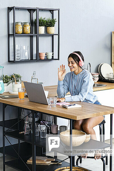Lächelnde junge Frau winkt während eines Videoanrufs auf dem Laptop zu Hause