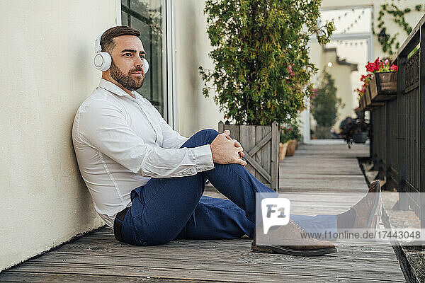 Businessman listening music while sitting near wall in office balcony