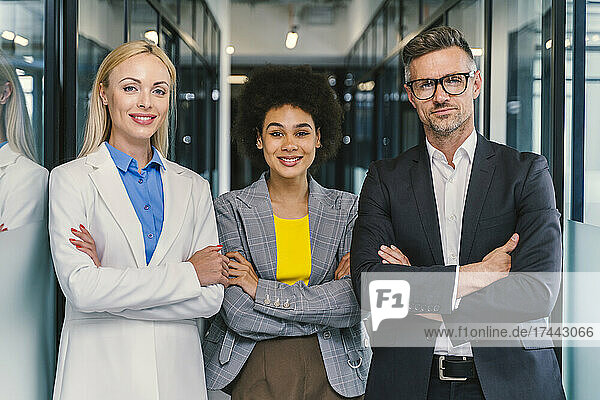 Multi-ethnic male and female business professionals standing with arms crossed in office
